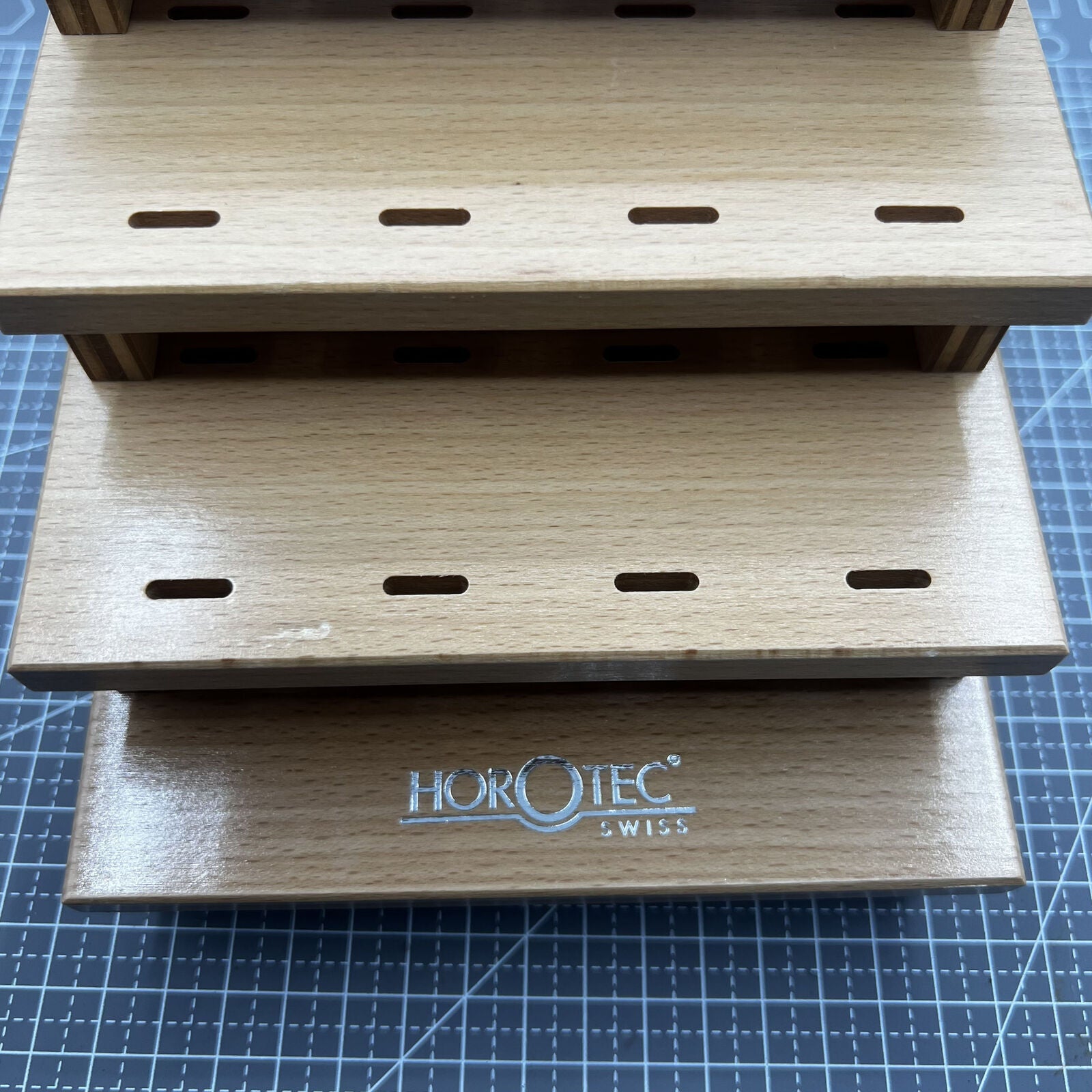 Swiss Horotec wooden rack storing 12 precision watchmaker tweezers for tidy tool organization.