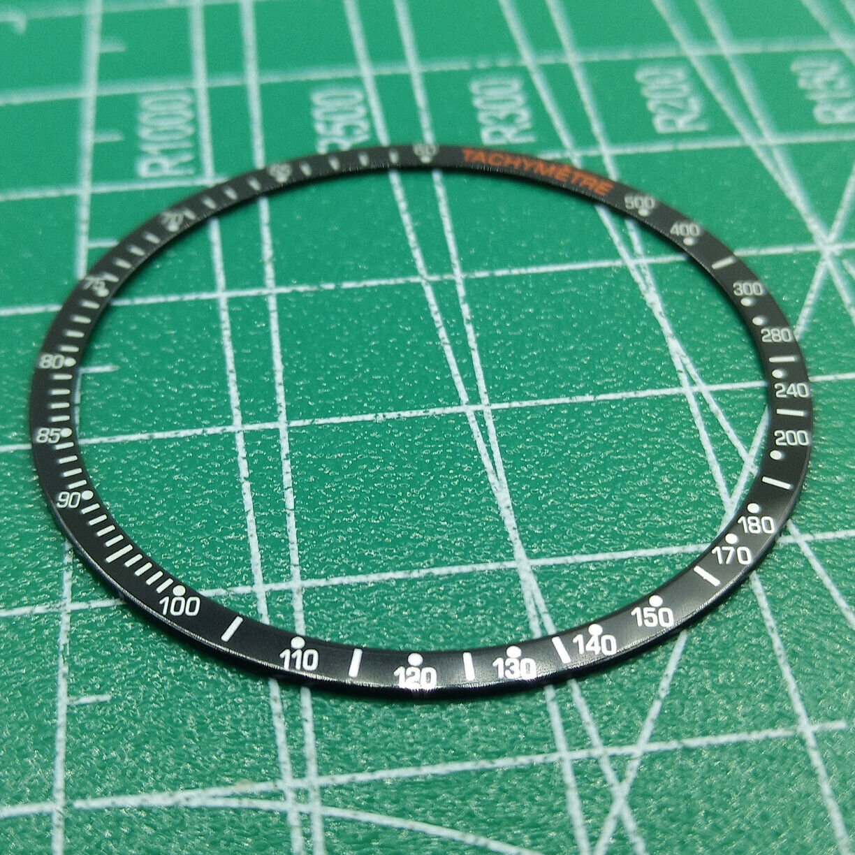 Black aluminum alloy watch bezel with white font, compatible with Omega Speedmaster models, durable replacement ring.