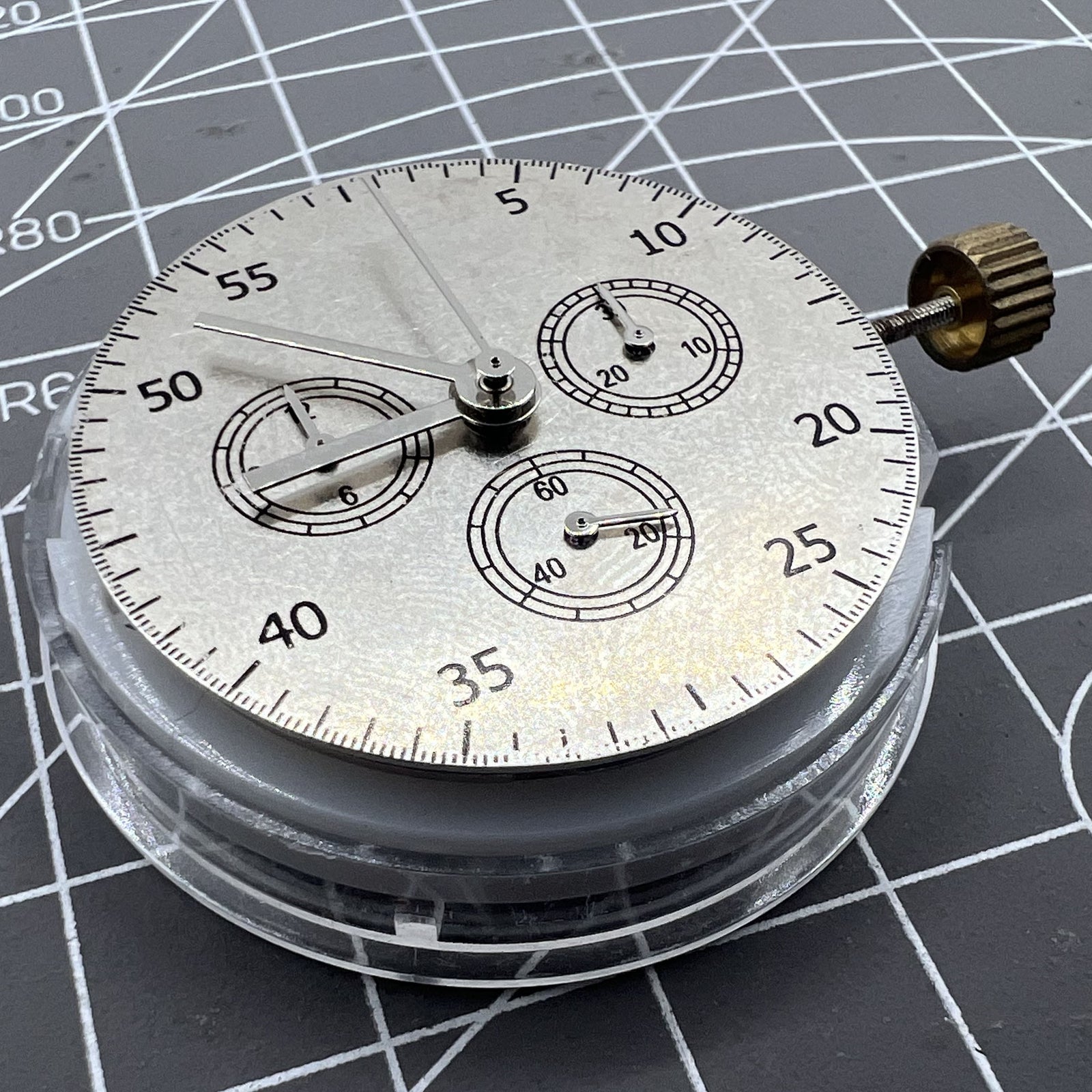 Close-up of China Made 7750 Automatic Chronograph Movement with ETA 7753 layout showing detailed gears at 3, 6, and 9 o'clock positions.