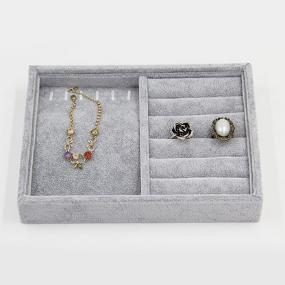 Gray velvet jewelry tray with grid compartments for stackable storage of watch accessories.