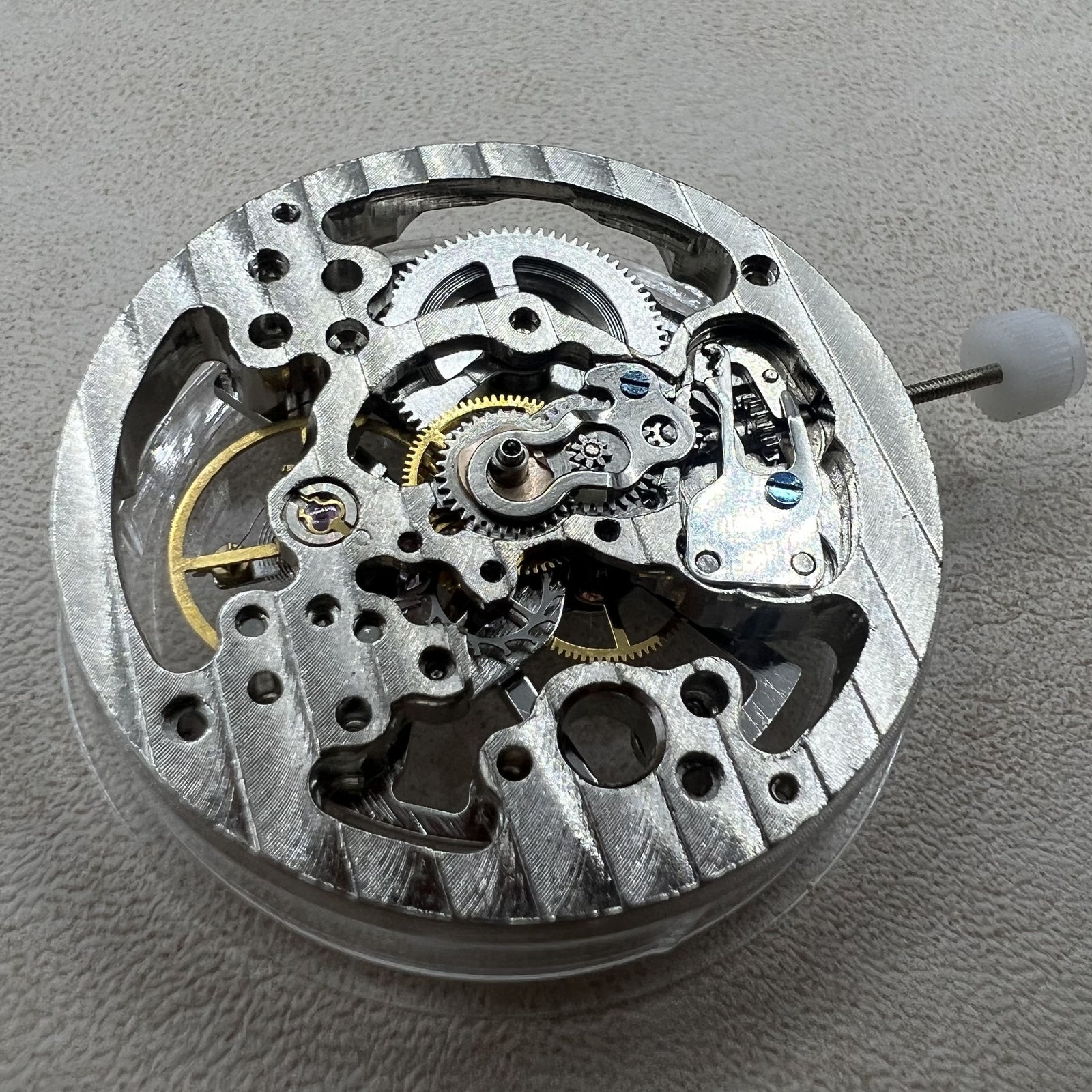Hollow silver manual winding watch movement displaying intricate gears and craftsmanship.