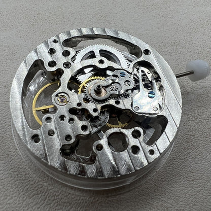 Hollow silver manual winding watch movement displaying intricate gears and craftsmanship.